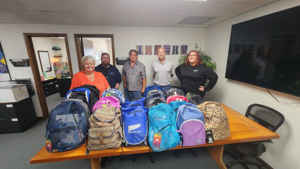 INSERV Community Outreach Team standing behind a table with backpacks put together with school supplies to be given away to team members with kids.