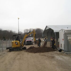 Environmental Services A construction crew using a mini excavator to dig and move a pile of dirt outside an industrial facility enclosure.