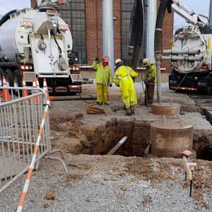 Hydro Excavation Services Daytime hydro excavation crew using pressure wands and vacuum truck hoses to safely expose underground utilities at an industrial work site.