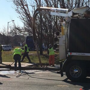 Hydro Excavation Services Utility crew performing hydro excavation near a paved sidewalk using a vacuum truck with an overhead boom hose.