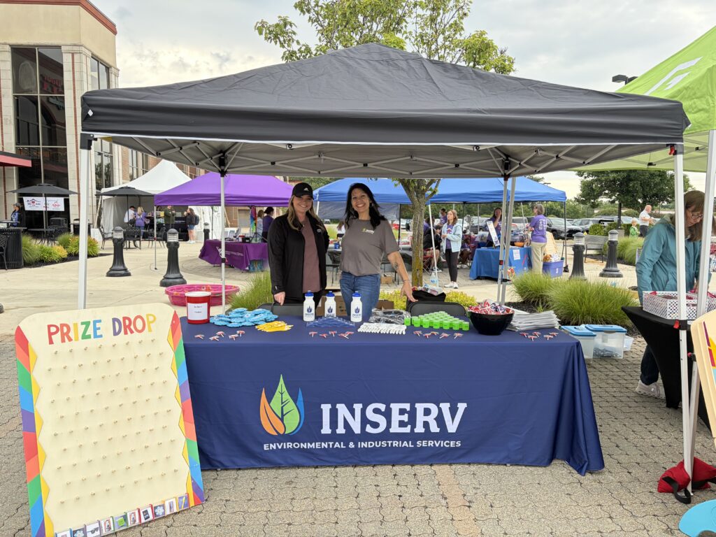 Two INSERV representatives smiling behind a branded event booth with promotional items and a peg drop game.