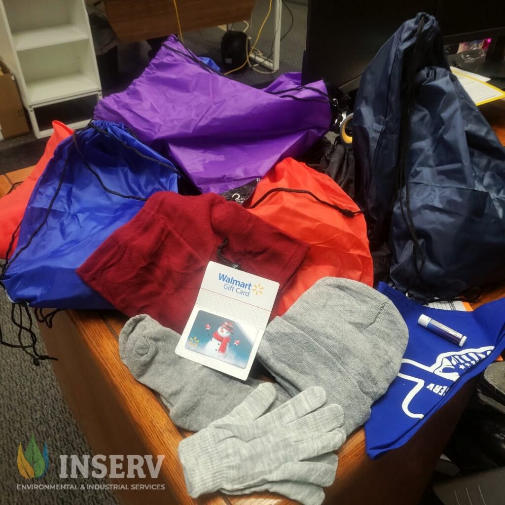 Several colorful drawstring backpacks, knit gloves, and beanies are spread across a wooden table, with a Walmart gift card and an INSERV logo visible.