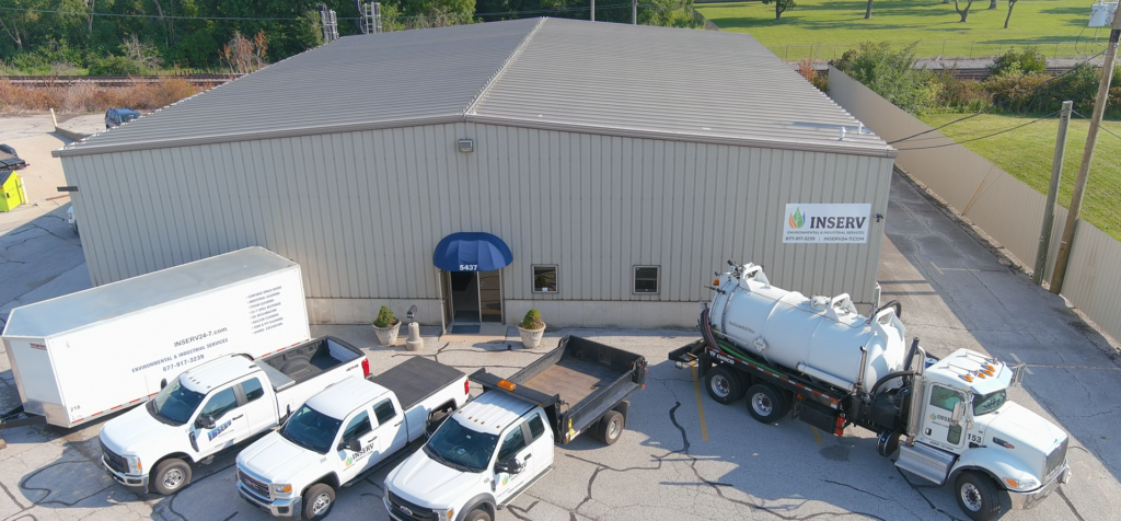 This image consists of a large grey building with a blue awning and an INSERV logo. There are several white trucks in the foreground.