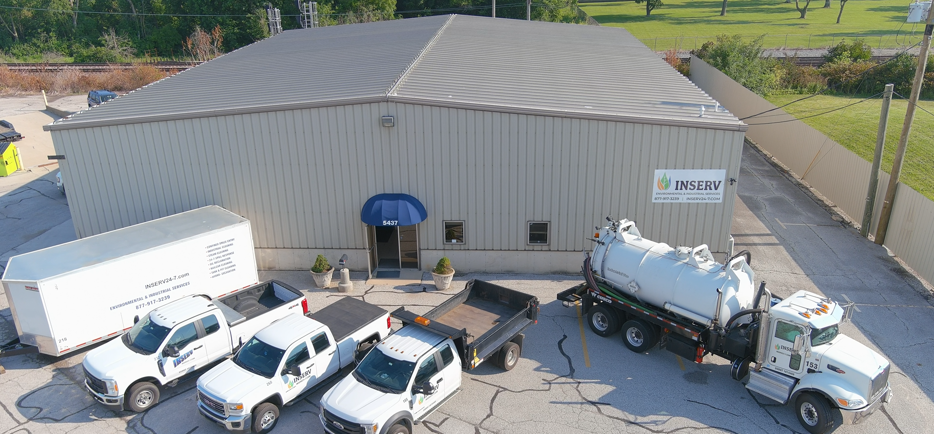 This image consists of a large grey building with a blue awning and an INSERV logo. There are several white trucks in the foreground.